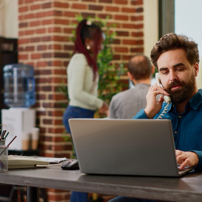 Company employee answering landline phone call at corporate job, talking to manager on office cord telephone line. Having remote conversation with phone number at work, business call.